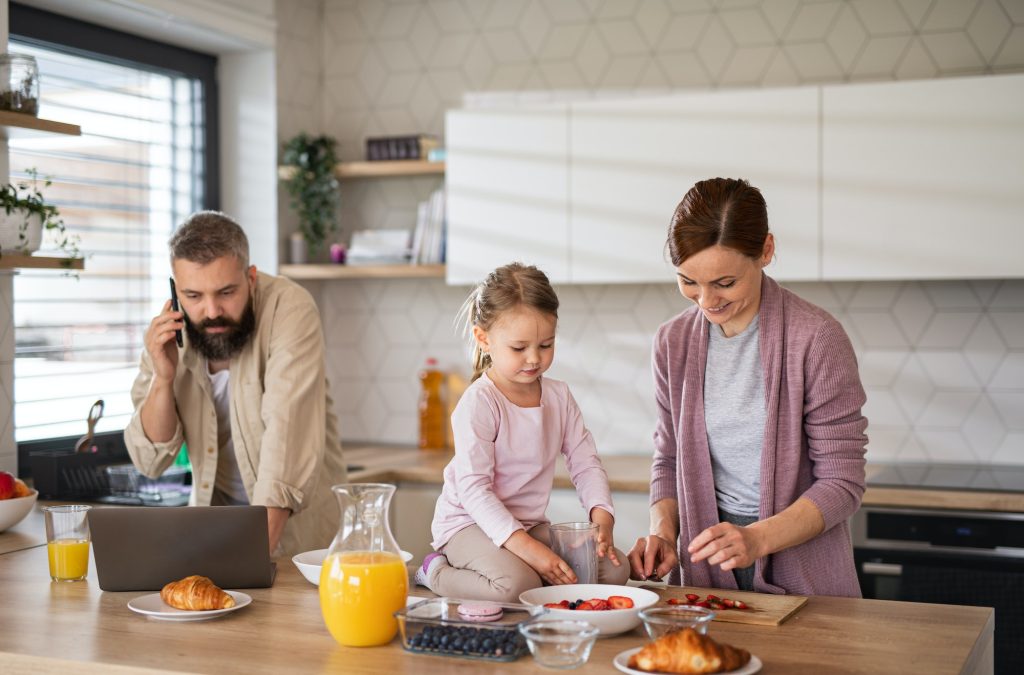 Family with small daughter indoors in kitchen, everyday life and home office with child concept.
